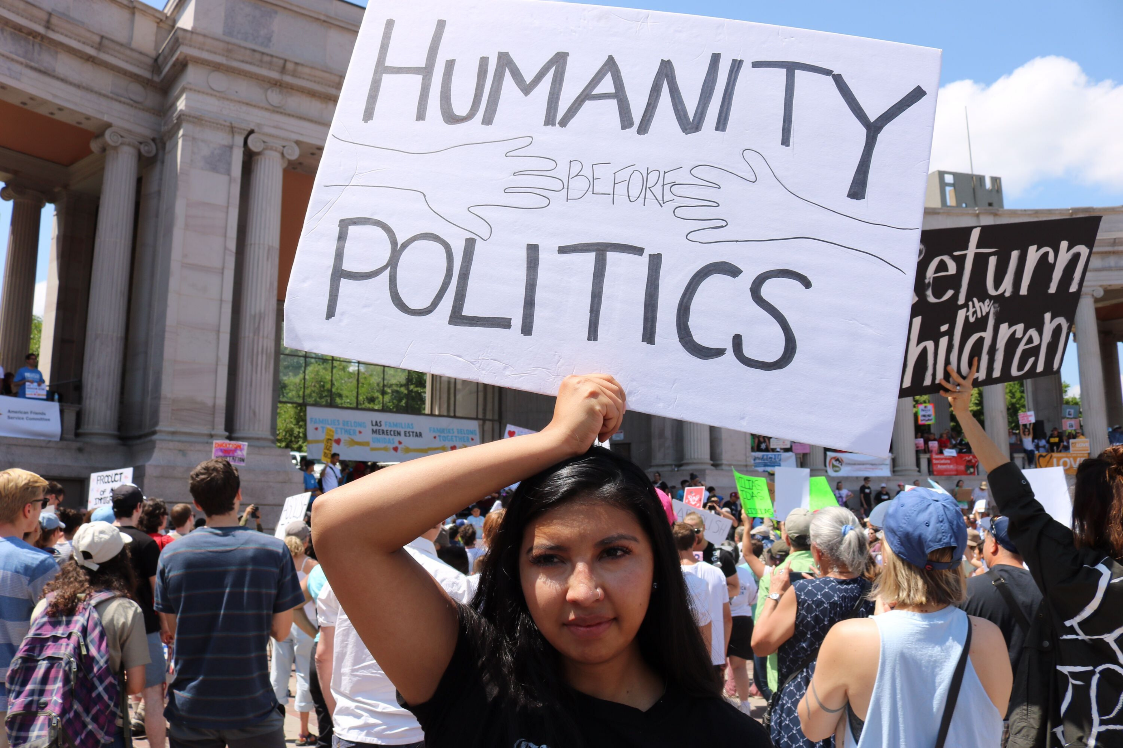 Image of a woman holding a sign at a rally that reads humanity before politics